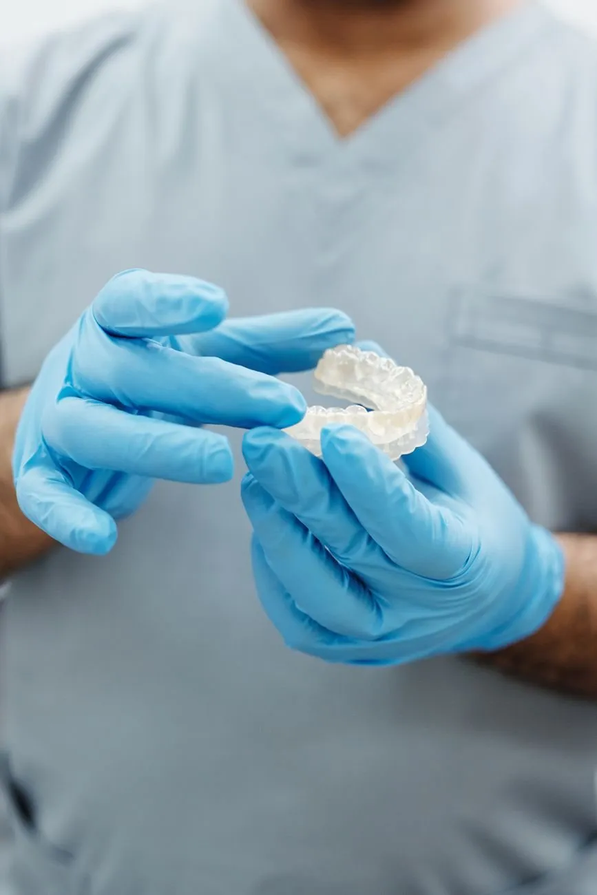 Gloved hands holding a clear aligner tray in front of blue scrubs