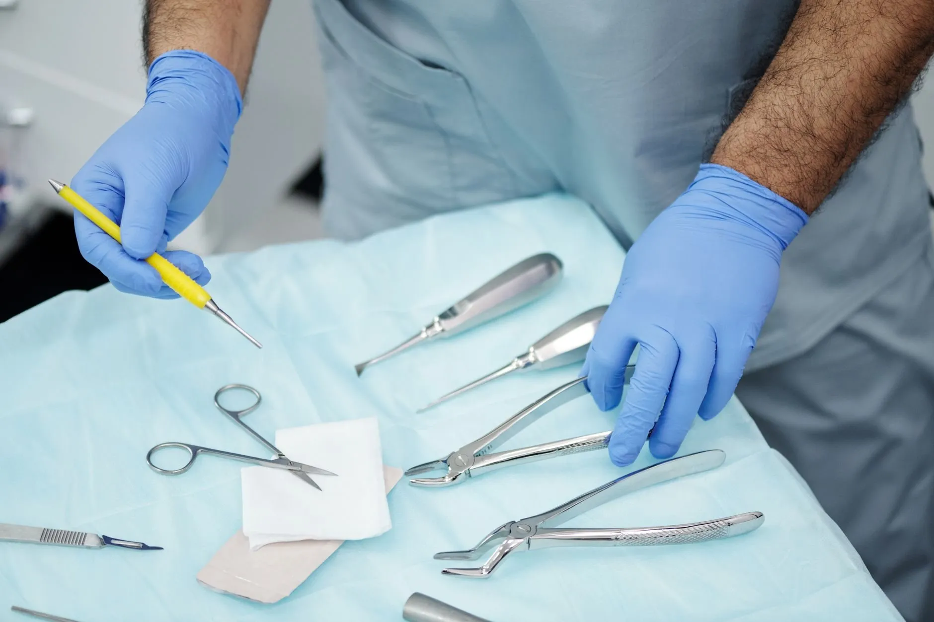 Gloved hands laying out instruments on a pale blue tray cover