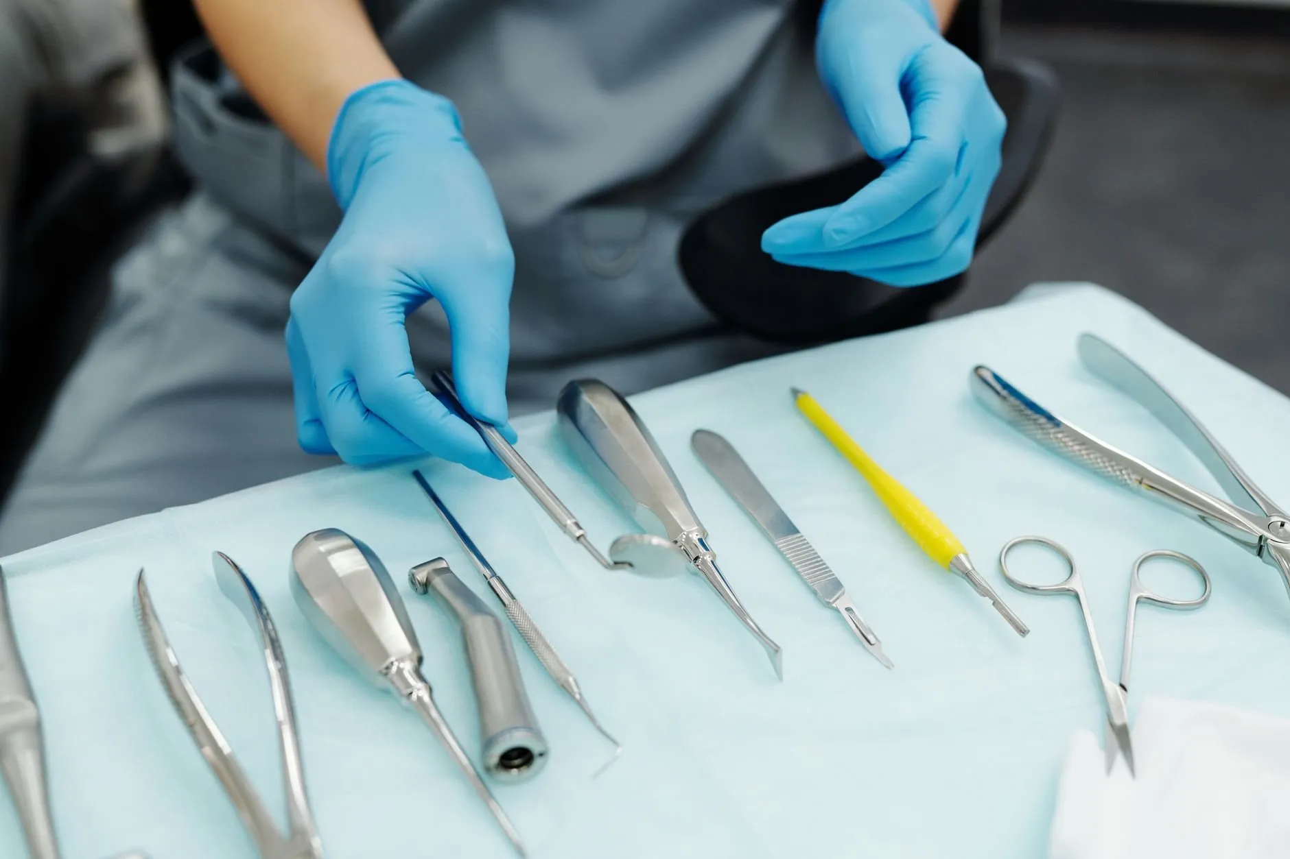 A gloved hand selecting an instrument from a neatly laid dental tray