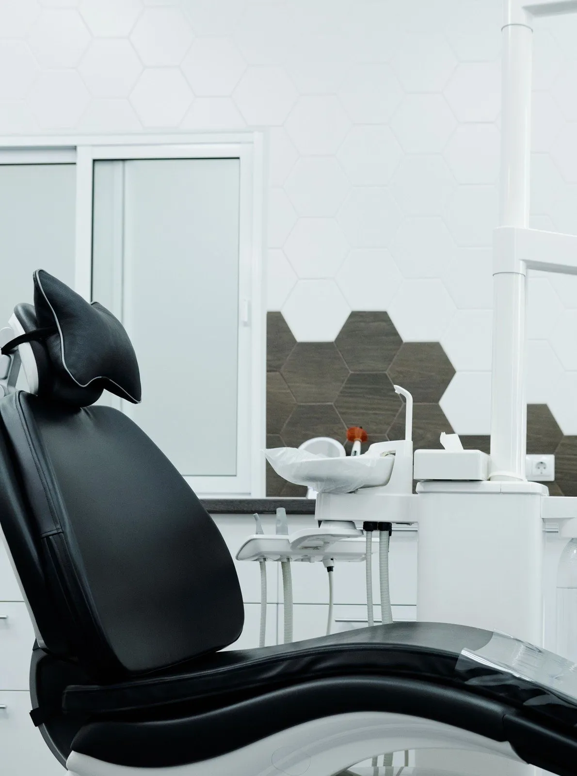 A black dental chair in a white treatment room with hexagonal wall tiles