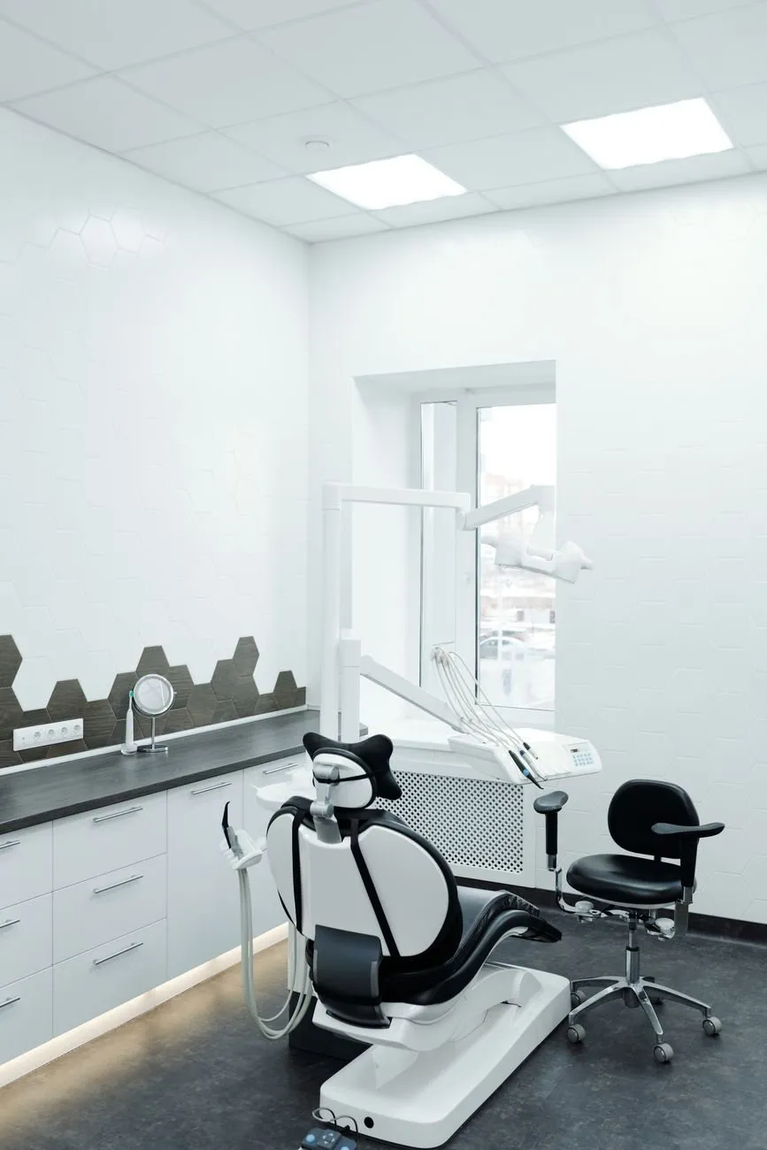 A small, bright treatment room with a dental chair and stool